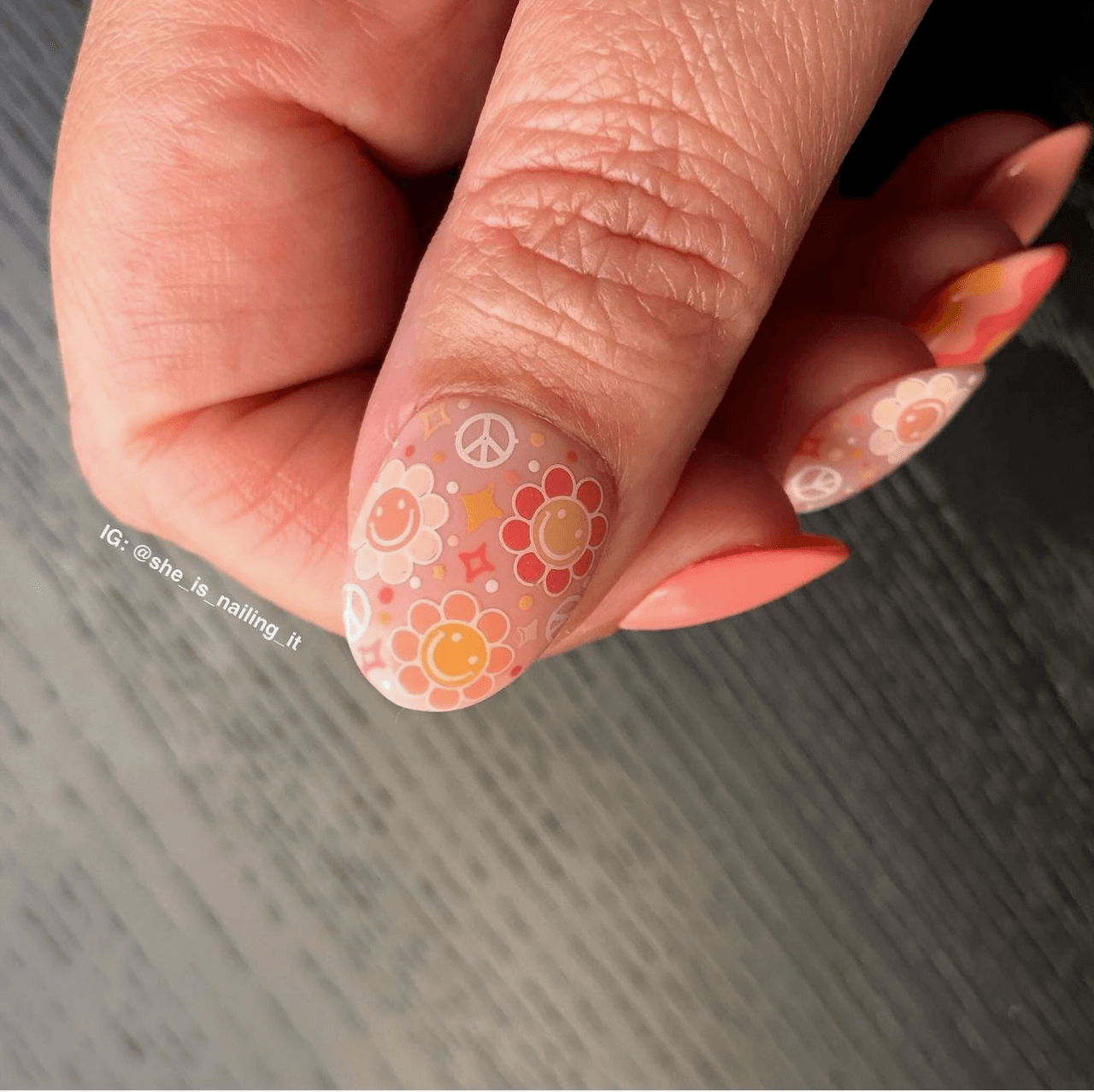 single-manicured-nail-with-layered-art-designs-of-smiling-flowers-and-peace-sign