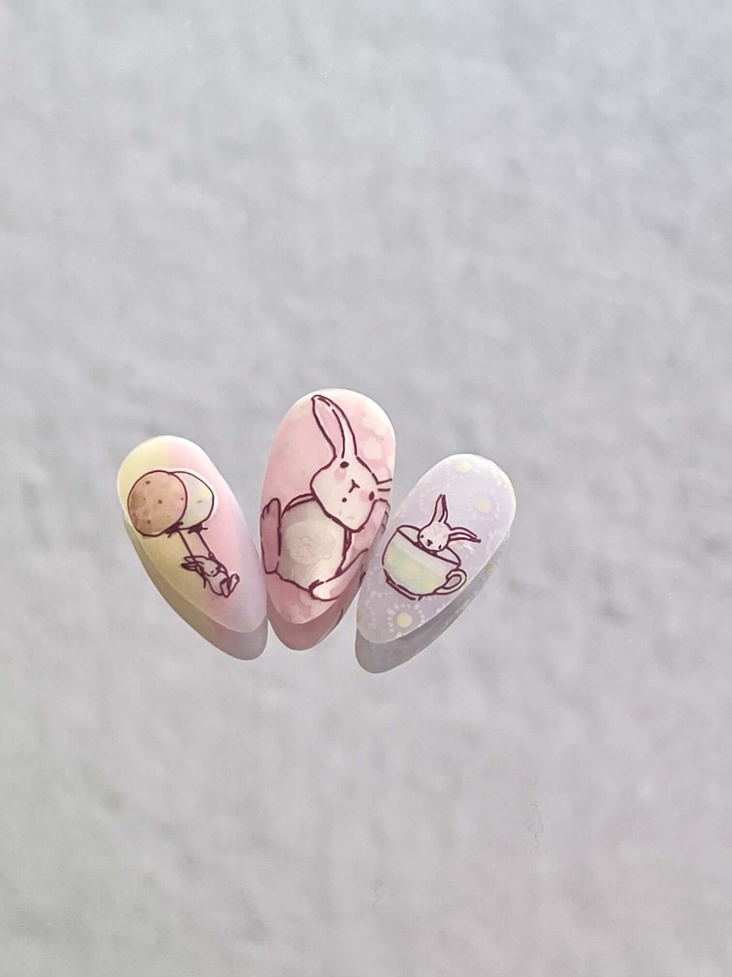 Three-manicured-nail-tips-showing-nail-art-designs-of-bunny-with-balloon-and-bunny-in-a-teacup