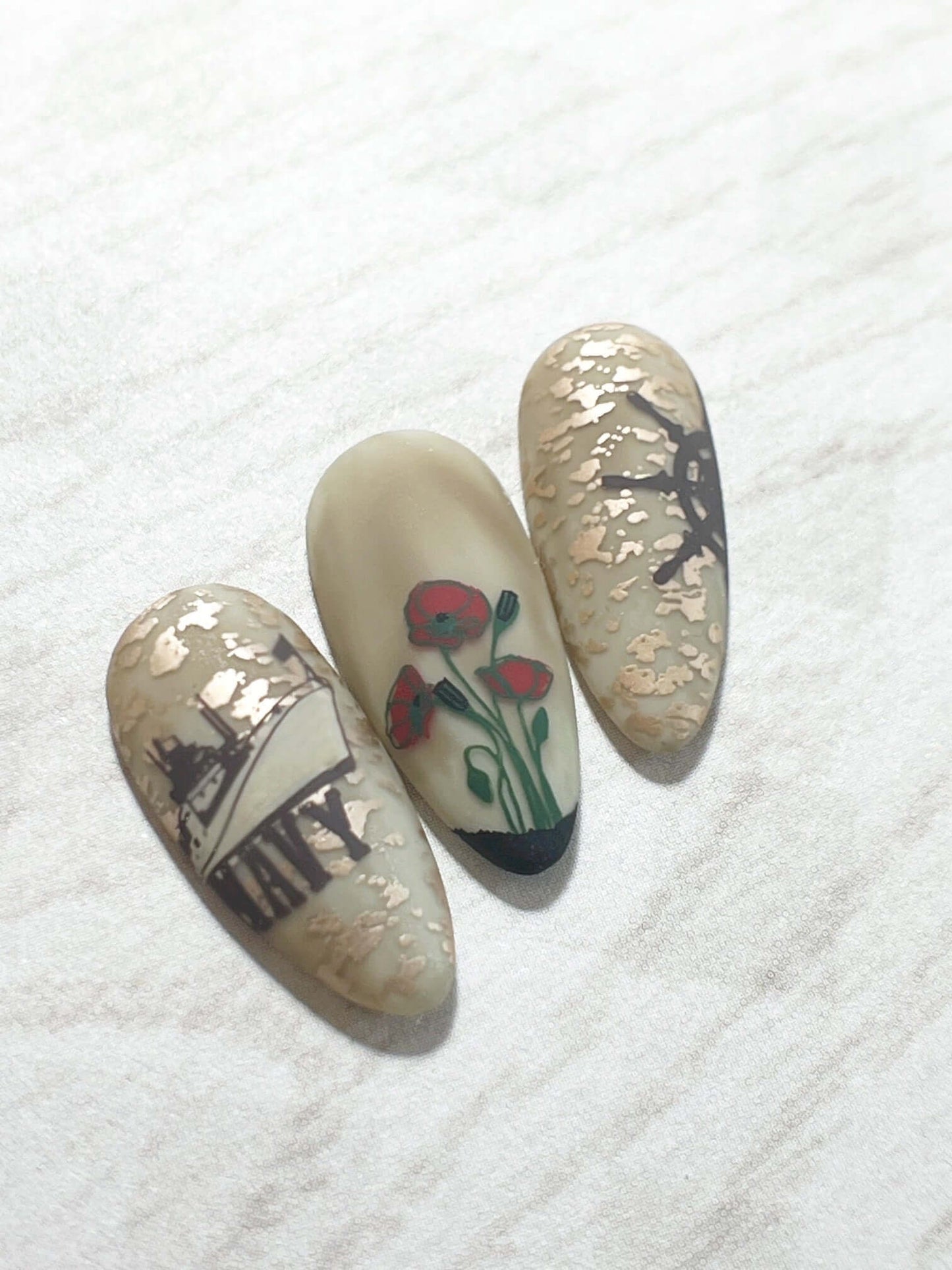 Three-nail-tips-showing-military-themed-nail-art-of-a-navy-ship-and-poppies
