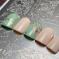 Set of green and beige nail polish samples on a textured surface