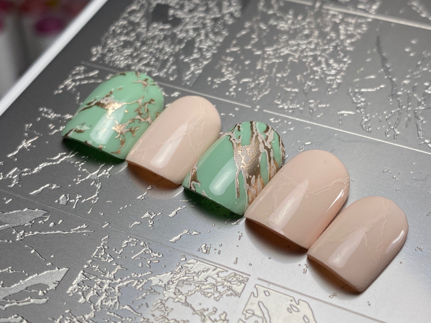 Set of green and beige nail polish samples on a textured surface