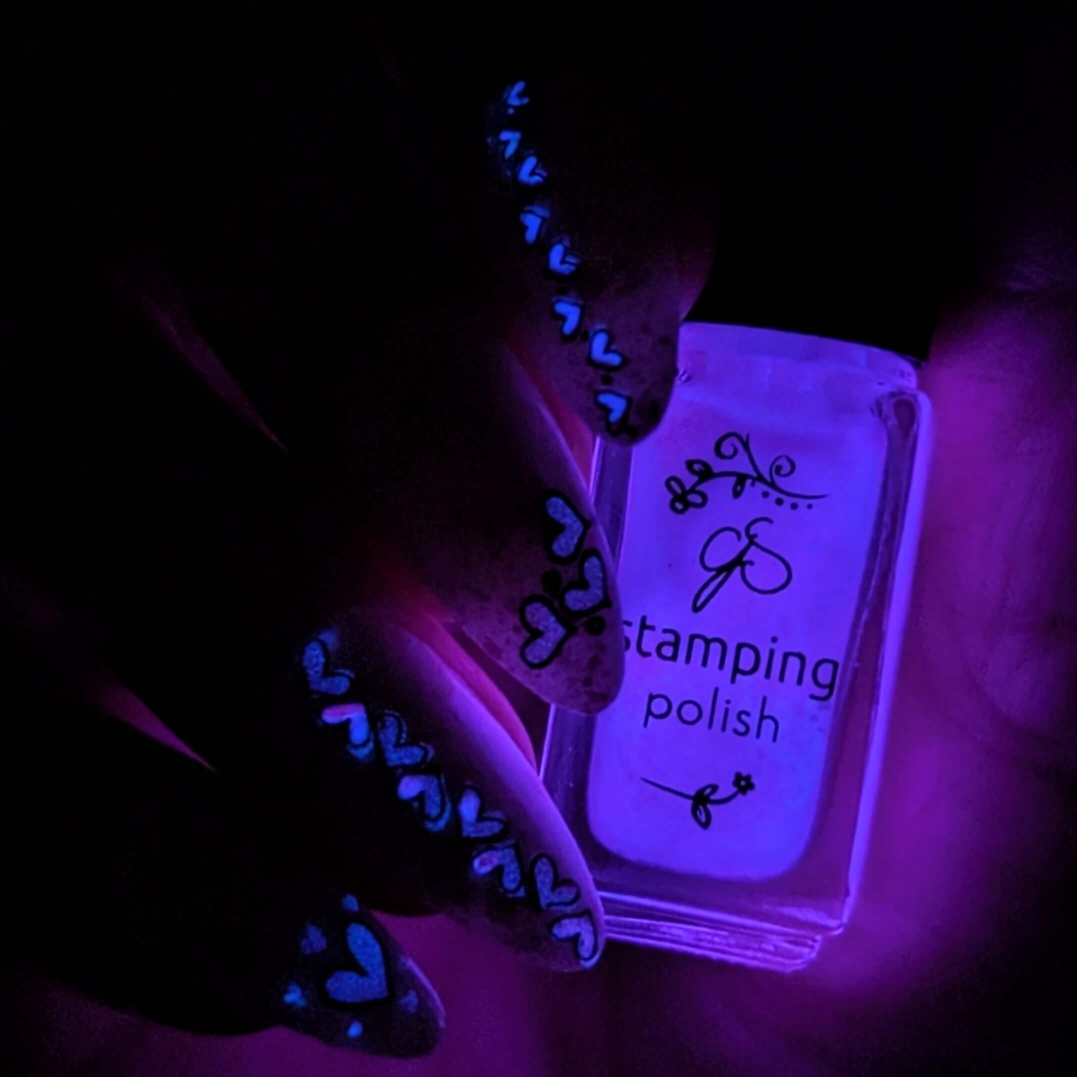 manicured-hand-with-nail-art-designs-of-little-cartoon-hearts-holding a bottle of-glow-in-the-dark-stamping-polish