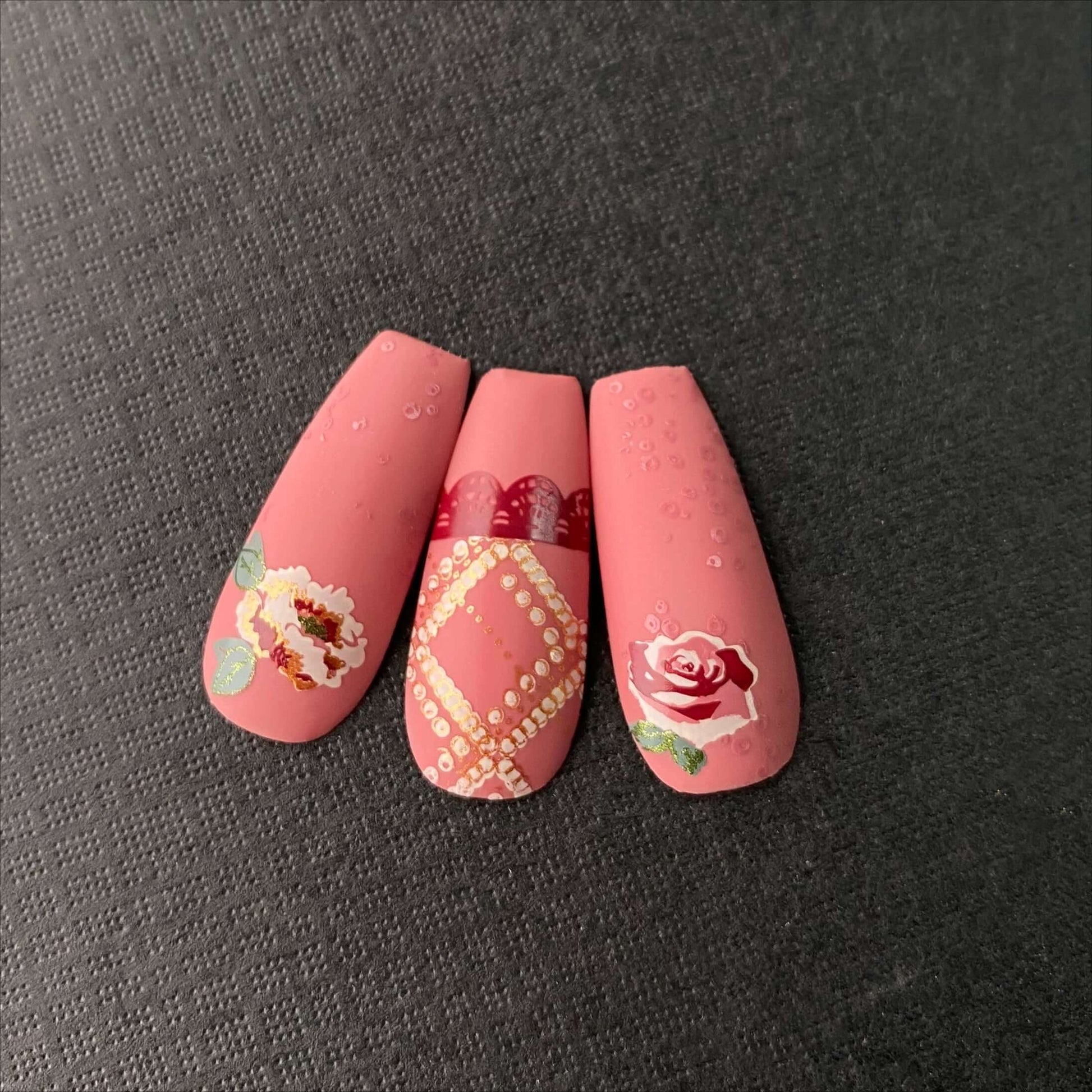 three-manicured-nail-tips-showing-layered-nail-art-designs-of-roses-lace-pattern