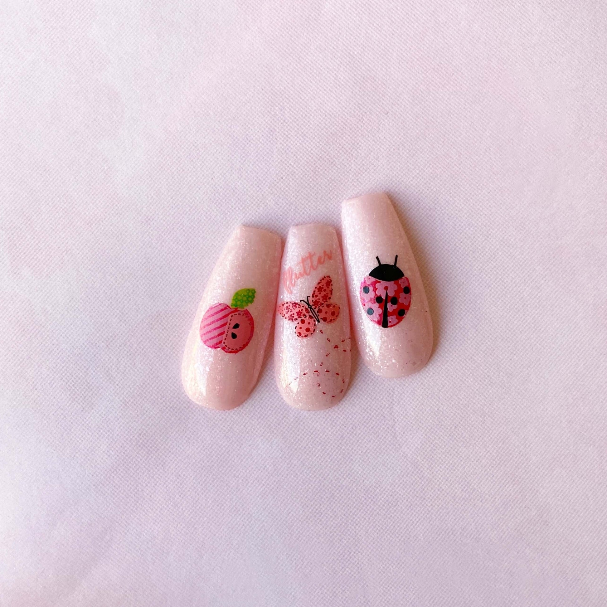 three-nail-tips-with-nail-art-designs-of-a-butterfly-ladybird-and-patchwork-apple